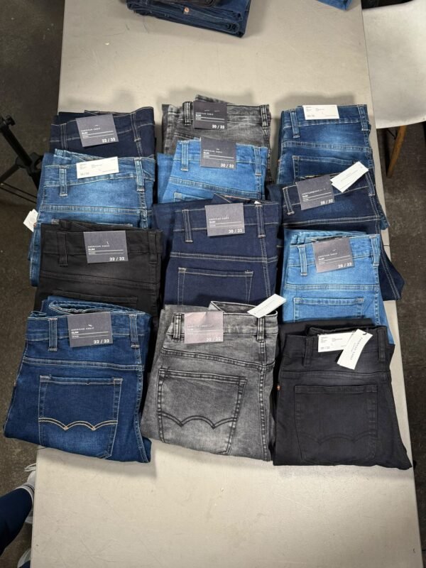 Doce pantalones de mezclilla doblados sobre una mesa, surtidos en azul, negro y gris
