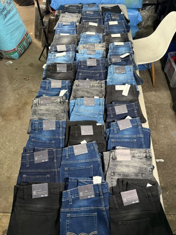 Treinta y seis pantalones de mezclilla doblados sobre una mesa larga, surtidos en azul, negro y gris