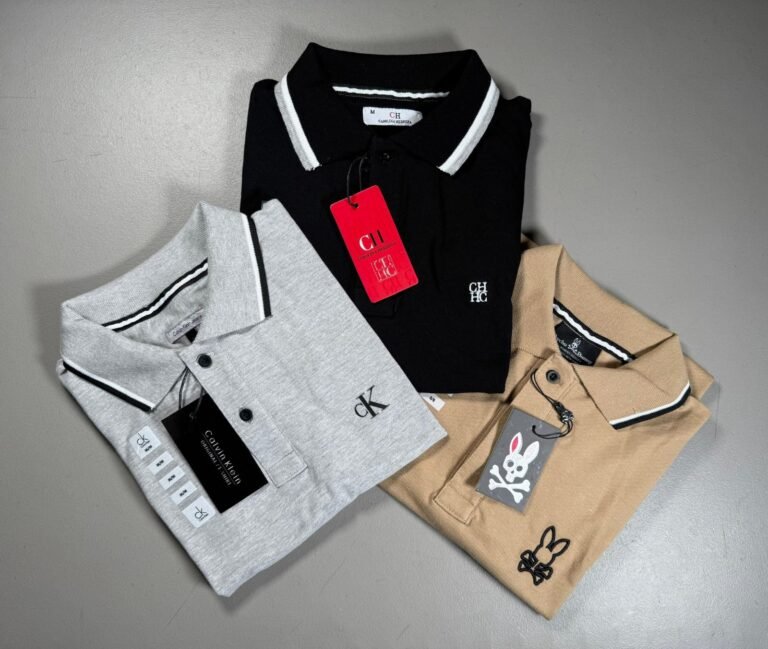 Playeras tipo polo dobladas en negro, gris y beige con etiqueta