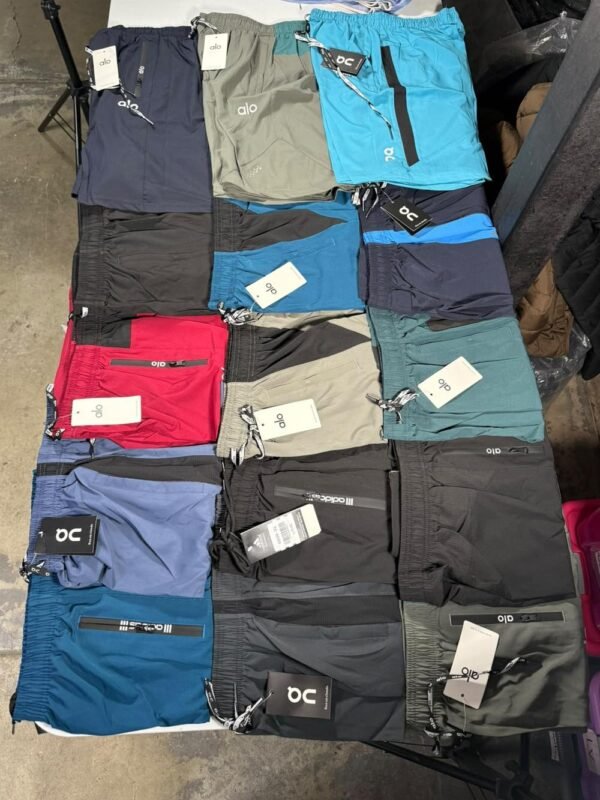 Quince shorts deportivos doblados sobre una mesa, surtidos en azul, verde, gris, negro y rojo, todos con etiqueta