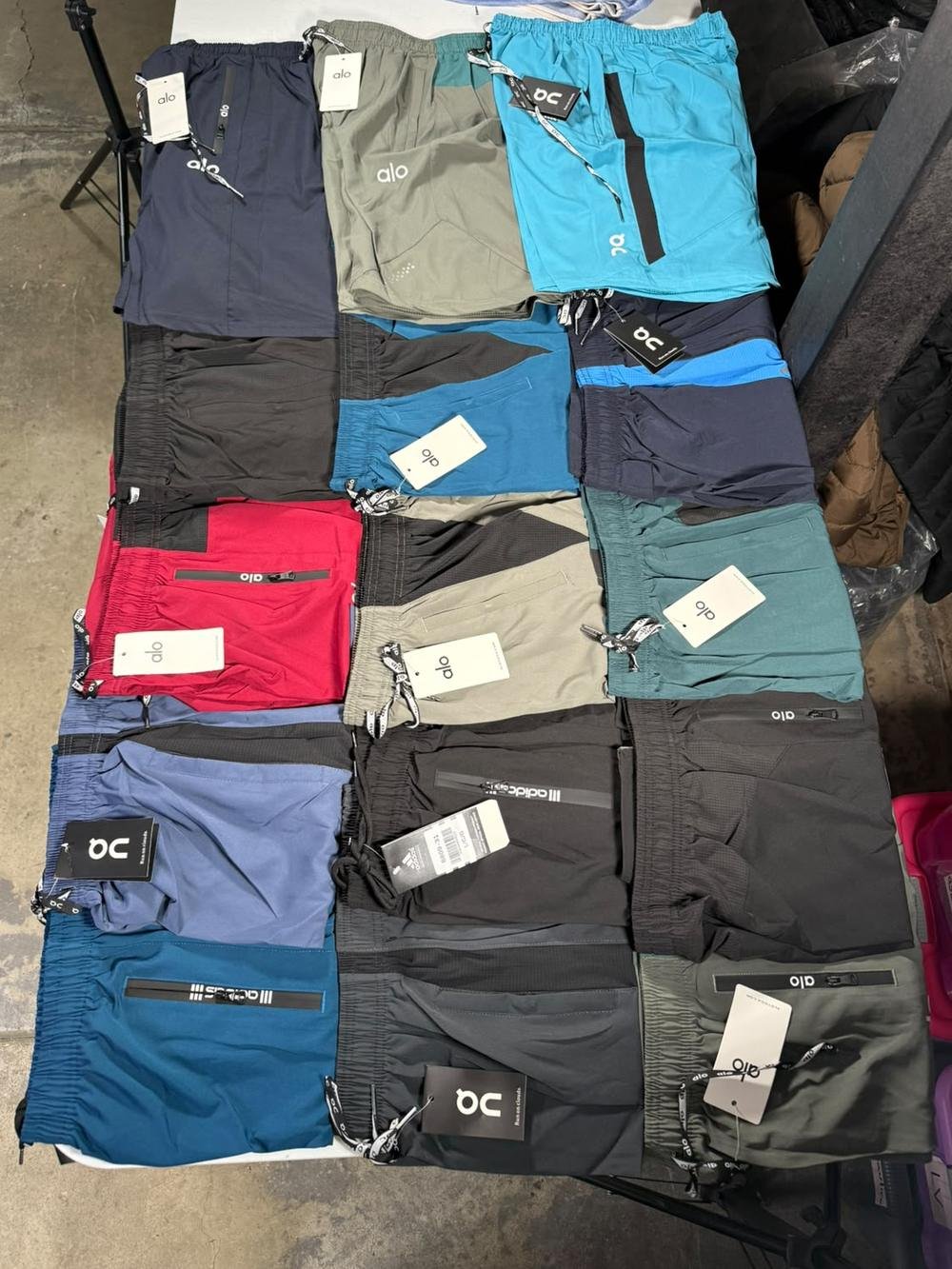 Quince shorts deportivos doblados sobre una mesa, surtidos en azul, verde, gris, negro y rojo, todos con etiqueta