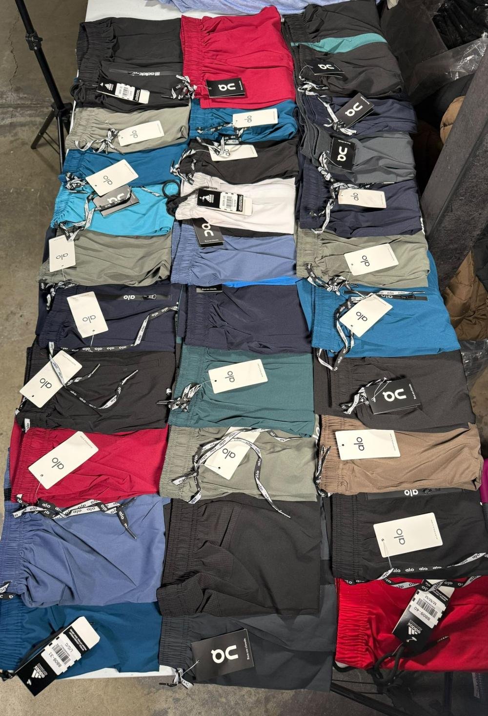 Treinta shorts deportivos doblados sobre una mesa, surtidos en azul, verde, rojo, gris y negro, todos con etiqueta