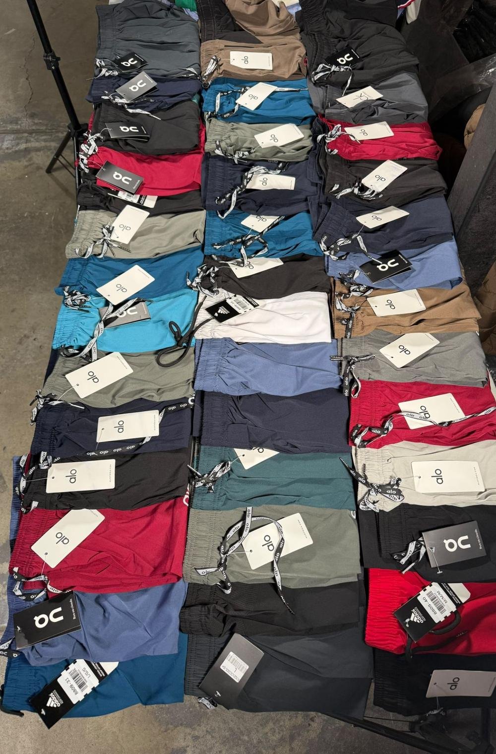 Mesa llena de shorts deportivos doblados, surtidos en azul, verde, rojo, gris, café y negro, todos con etiqueta
